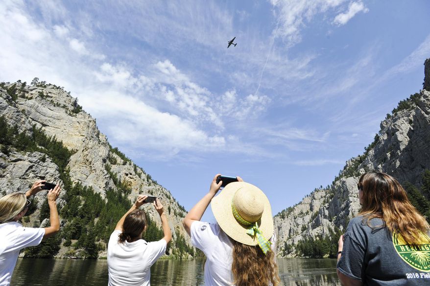 Spectators use cell phones to capture Miss Montana fly over and drop wreaths Monday, Aug. 5, 2019, in the Gates of the Mountains in Montana. The plane dropped twelve wreaths commemorating the twelve smokejumpers who died fighting the Mann Gulch Fire 70 years ago. (Thom Bridge/Independent Record via AP)
