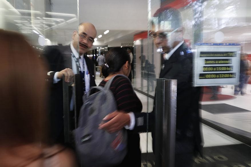 Security personnel guard the front door of a building that houses the federal mint's headquarters in Mexico City, Tuesday, Aug. 6, 2019. Mexican authorities say gunmen raided the federal mint's headquarters and took items from a vault. An official says the gunmen got away with gold coins, commemorative watches and other valuables. He didn't put a value on the loss, but local media say the stolen items are worth up to 50 million pesos ($2.5 million). (AP Photo/Marco Ugarte)