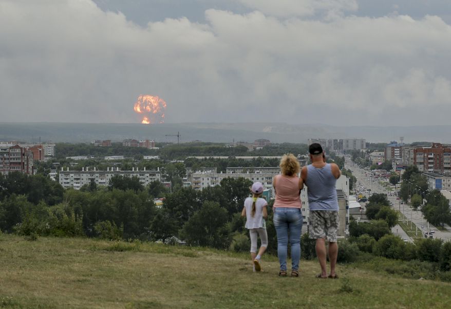 In this photo taken on Monday, Aug. 5, 2019, a family watches explosions at a military ammunition depot near the city of Achinsk in eastern Siberia's Krasnoyarsk region, in Achinsk, Russia. Russian officials say powerful explosions at a military depot in Siberia left 12 people injured and one missing and forced over 16,500 people to leave their homes. (AP Photo/Dmitry Dub)