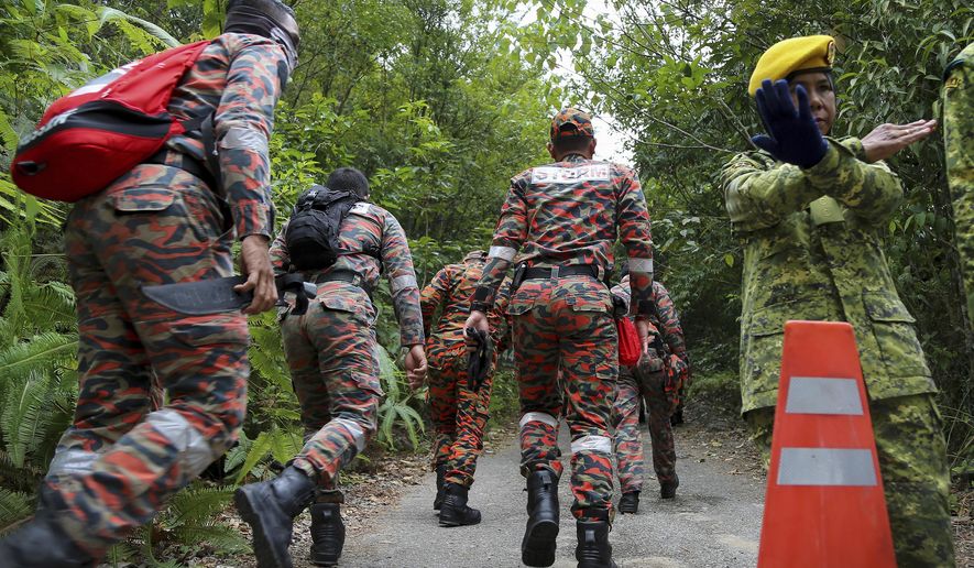 A member of the People's Volunteer Corps (RELA) gestures to journalists as members of rescue team enter a forest to conduct a search operation for a missing British girl, in Seremban, Malaysia, Wednesday, Aug. 7, 2019. A 15-year-old London girl disappeared from a Malaysian resort over the weekend, with the girl's family saying they believe she was abducted and police saying there was no indication that had happened. (AP Photo/Annice Lyn)