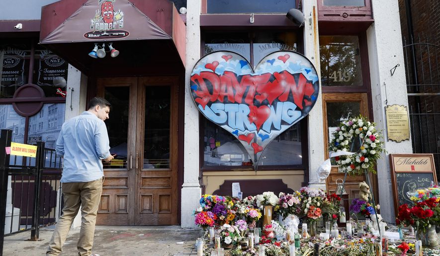A pedestrian passes a makeshift memorial for the slain and injured victims of a mass shooting that occurred in the Oregon District early Sunday morning, Wednesday, Aug. 7, 2019, in Dayton, Ohio. President Donald Trump headed to Dayton and El Paso, Texas on Wednesday to offer a message of healing and unity, but he will be met by unusual hostility in both places by people who fault his own incendiary words as a contributing cause to the mass shootings . (AP Photo/John Minchillo)