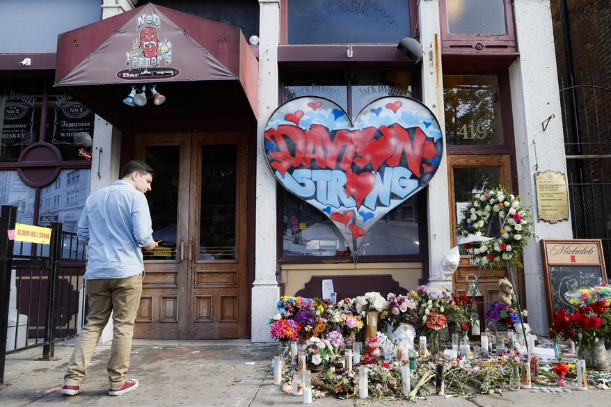 A pedestrian passes a makeshift memorial for the slain and injured victims of a mass shooting that occurred in the Oregon District early Sunday morning, Wednesday, Aug. 7, 2019, in Dayton, Ohio. President Donald Trump headed to Dayton and El Paso, Texas on Wednesday to offer a message of healing and unity, but he will be met by unusual hostility in both places by people who fault his own incendiary words as a contributing cause to the mass shootings . (AP Photo/John Minchillo)