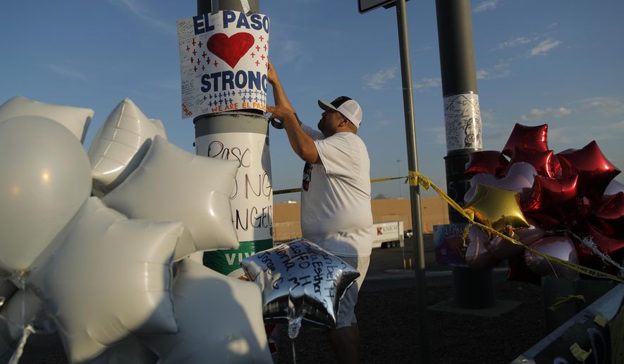 A man hangs up an "El Paso Strong" sign at a makeshift memorial at the scene of a mass shooting at a shopping complex, Tuesday, Aug. 6, 2019, in El Paso, Texas. (AP Photo/John Locher)