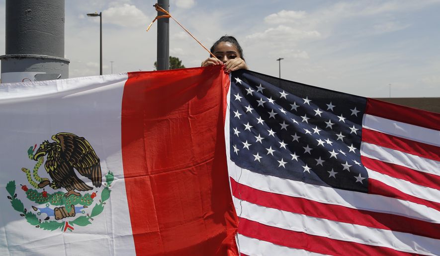 Maylin Reyes hangs a Mexican flag at a makeshift memorial near the scene of a mass shooting at a shopping complex Monday, Aug. 5, 2019, in El Paso, Texas. (AP Photo/John Locher)