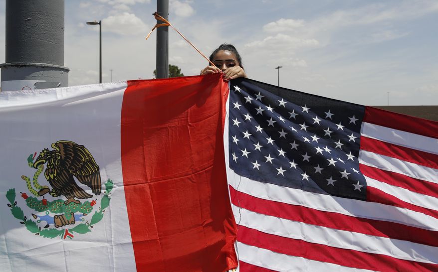 Maylin Reyes hangs a Mexican flag at a makeshift memorial near the scene of a mass shooting at a shopping complex Monday, Aug. 5, 2019, in El Paso, Texas. (AP Photo/John Locher)