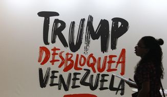 A woman walks next to a sign that reads in Spanish &amp;quot;Trump, Unblock Venezuela,&amp;quot; a reference to the Venezuelan government view that U.S. sanctions, aimed at toppling President Nicolas Maduro, are driving the country&#39;s economic problems, at the Sao Paulo Forum in Caracas, Venezuela, Friday, July 26, 2019. (AP Photo/Leonardo Fernandez)