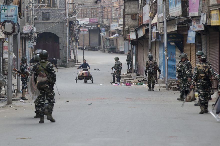 In this Tuesday, Aug. 6, 2019 photo, a Kashmiri municipal worker pushes his cart filled with trash as Indian paramilitary soldiers patrol during curfew in Srinagar, Indian controlled Kashmir, Wednesday, Aug. 7, 2019. Authorities in Hindu-majority India clamped a complete shutdown on Kashmir as they scrapped the Muslim-majority state's special status, including exclusive hereditary rights and a separate constitution, and divided it into two territories. (AP Photo/Dar Yasin)