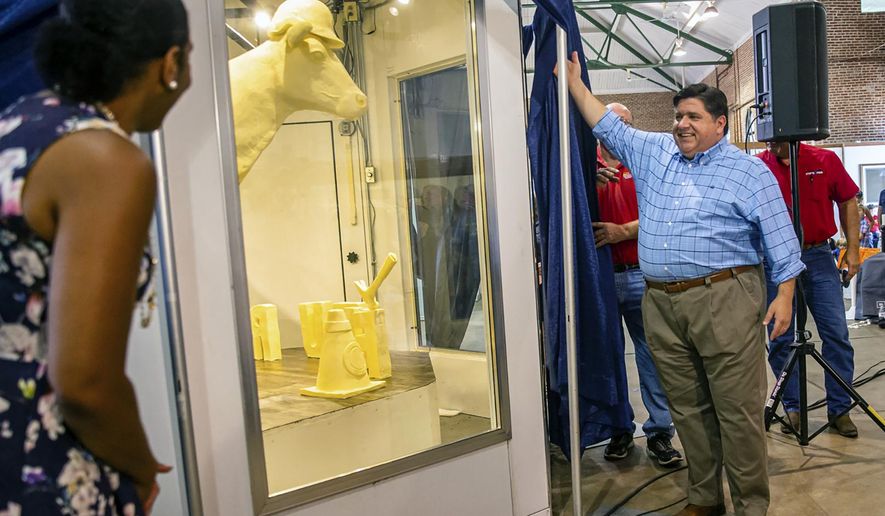 Illinois Gov. JB Pritzker, center, and Illinois Lt. Gov. Juliana Stratton, left, unveil the 2019 Illinois State Fair Butter Cow during a ceremony inside the Dairy Building on the Illinois State Fairgrounds, Wednesday, Aug. 7, 2019, in Springfield, Ill. The theme of this year's butter cow, made of 800 pounds of recycled butter by artist Sarah Pratt, is "Building Our Future" and contains nine hearts hidden within the sculpture that represent the essential nutrients found in dairy products. (Justin L. Fowler/The State Journal-Register via AP)