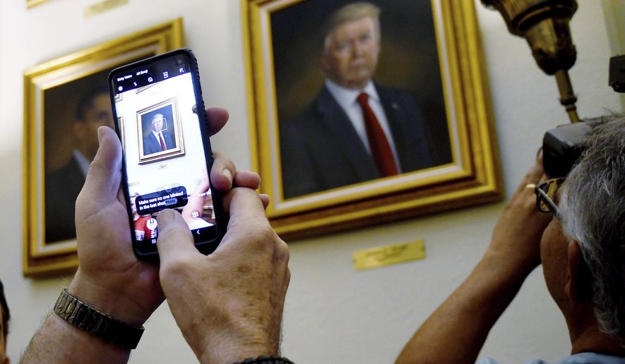 FILE - In this Aug. 1, 2019 file photo, people take photos of President Donald Trump's portrait hanging in the Colorado Capitol after an unveiling ceremony in Denver. On Friday, Aug. 9, 2019, The Associated Press reported on a manipulated video circulating online incorrectly asserting that the painting of Obama, left, fell off the wall as Trump’s was unveiled. (AP Photo/Thomas Peipert)