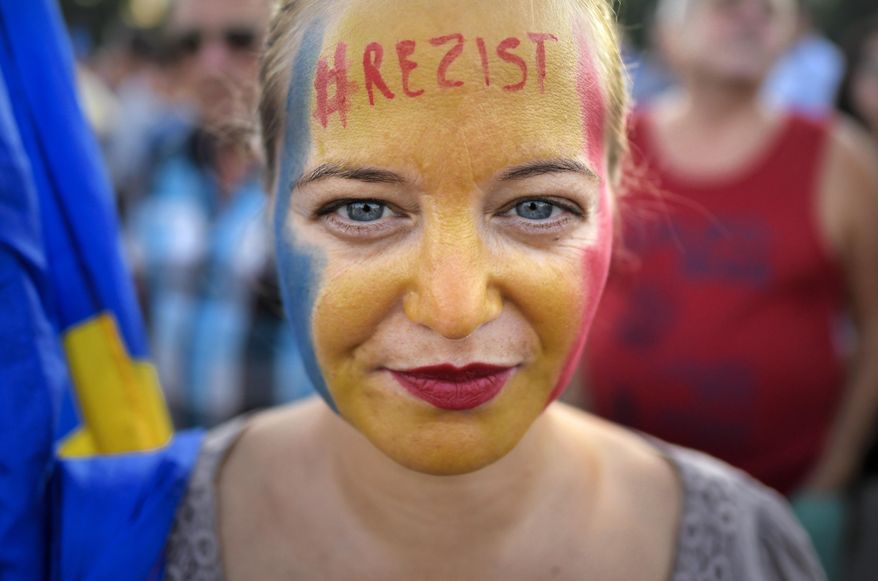 A woman with the Romanian flag colors and the word "Resist" painted on her face takes part in an anti-government protest in Victoria Square, outside the government headquarters in Bucharest, Romania, Saturday, Aug. 10, 2019. Thousands joined a protest, demanding the resignation of the government, one year after a similar rally turned violent and left dozens of participants and members of the riot police injured.(AP Photo/Andreea Alexandru)