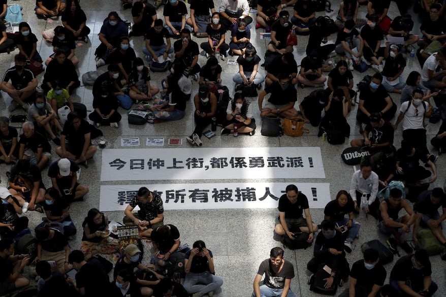 THIS ADDS TO CLARIFY THE TRANSLATION - Protesters surround banners that read: "Those on the street today are all warriors!" top, and "Release all the detainees!" during a sit-in rally at the arrival hall of the Hong Kong International airport, Monday, Aug. 12, 2019. Hong Kong police showed off water cannons Monday as pro-democracy street protests stretched into their 10th week with no sign of either side backing down. (AP Photo/Vincent Thian)