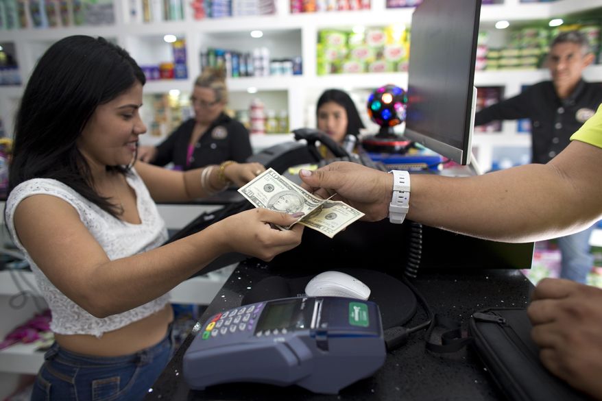A man pays for his purchases with U.S dollars at a store in Caracas, Venezuela, Friday, Aug. 9, 2019. A number of trendy shops packed with imported consumer goods have popped up in the last few months across Caracas while socialist authorities look the other way as the greenback has replaced the worthless local currency, the bolivar, as an accepted form of payment. (AP Photo/Ariana Cubillos)