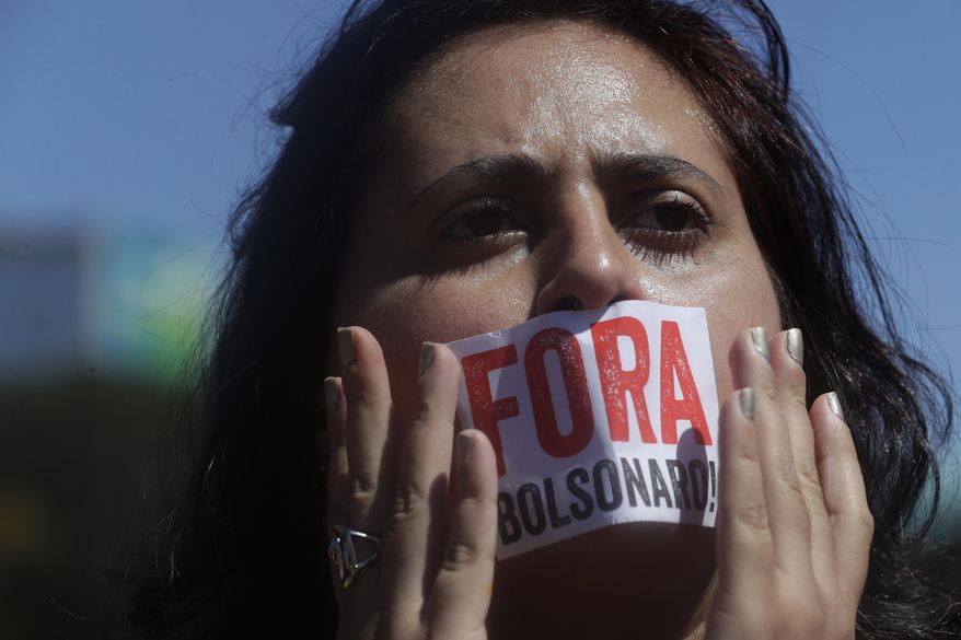 A teacher covers her mouth with a sticker that reads in Portuguese "Bolsonaro out!" in reference to Brazil's President Jair Bolsonaro, during a national strike against cuts in the education budget, in Brasilia, Brazil, Tuesday, Aug. 13, 2019. Union leaders have called for a strike in the education sector, to denounce the government’s budget freeze for public higher education and plans to open federal universities to private investment. (AP Photo/Eraldo Peres)