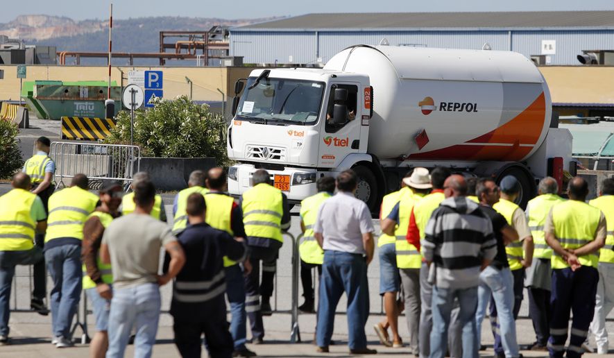 Tanker truck drivers on strike watch a fellow driver leaving a fuel depot in Aveiras, outside Lisbon, Monday, Aug. 12, 2019. Portugal is rationing gas as a precaution after some 2,000 tanker truck drivers began an open-ended strike over pay on Monday. (AP Photo/Armando Franca)
