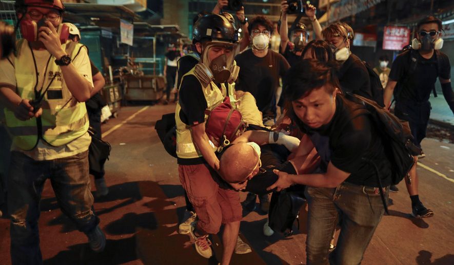 Medical staff and protesters carry an injured man as they face off with police near the Shum Shui Po police station in Hong Kong on Wednesday. Police fired tear gas at the protesters. Meanwhile, five people were arrested over violence at the airport. (Associated Press)