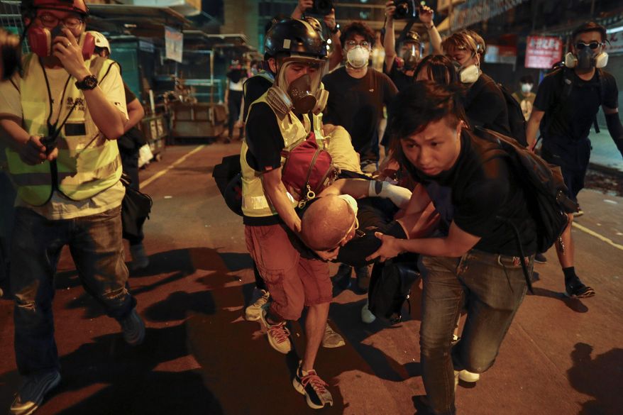 Medical staff and protesters carry an injured man as they face off with police near the Shum Shui Po police station in Hong Kong on Wednesday. Police fired tear gas at the protesters. Meanwhile, five people were arrested over violence at the airport. (Associated Press)