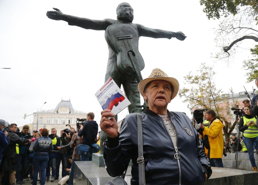 An opposition activist holds the Russian Constitution book in front of the monument to Soviet-era opposition legendary bard Vladimir Vysotsky during a protest in the center of Moscow, Russia, Saturday, Aug. 17, 2019. People rallied Saturday against the exclusion of some city council candidates from Moscow's upcoming election. (AP Photo/Alexander Zemlianichenko)