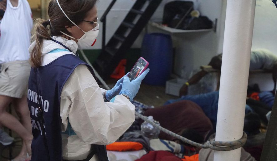 A Ministry of Health worker takes photos of migrants on the deck of the Open Arms Spanish humanitarian boat off the coast of the Sicilian island of Lampedusa, southern Italy, Sunday, Aug.18, 2019. (AP Photo/Francisco Gentico)