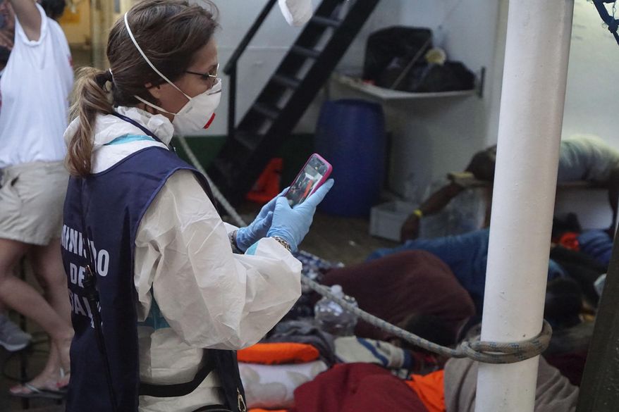 A Ministry of Health worker takes photos of migrants on the deck of the Open Arms Spanish humanitarian boat off the coast of the Sicilian island of Lampedusa, southern Italy, Sunday, Aug.18, 2019. (AP Photo/Francisco Gentico)