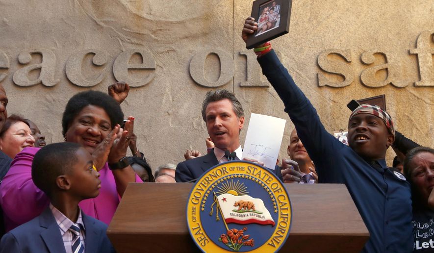 Gov. Gavin Newsom holds up the measure by Assemblywoman Shirley Weber, D-San Diego, left, that he signed that limits the use of lethal force by law enforcement Sacramento, Calif., Monday, Aug. 19, 2019. Weber's bill, AB392, would bar police from using lethal force unless it is necessary to prevent imminent threat of death or serious injury to themselves and others. Stevante Clark, right, holds up a photo of his brother, Stephon Clark, who was shot and killed by Sacramento Police in 2018. (AP Photo/Rich Pedroncelli)