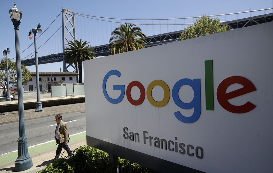 FILE - In this May 1, 2019, file photo a man walks past a Google sign outside with a span of the Bay Bridge at rear in San Francisco.  (AP Photo/Jeff Chiu, File)