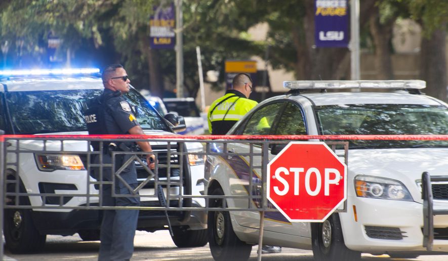 Law enforcement personnel stand with weapons near two LSU police vehicles parked in between the LSUU Student Union and Coates Hall, in New Orleans after the all-clear on a possible armed intruder in Coates Hall, Tuesday, August 20, 2019.  (Travis Spradling/The Advocate via AP)