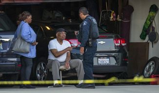 An Ontario Police officer interviews a neighbor sitting in his garage next door to a home where two children, an infant and a teenager, were found dead with their mother, who was unresponsive, Tuesday, Aug. 20, 2019, in Ontario, Calif. (Terry Pierson/The Orange County Register via AP)