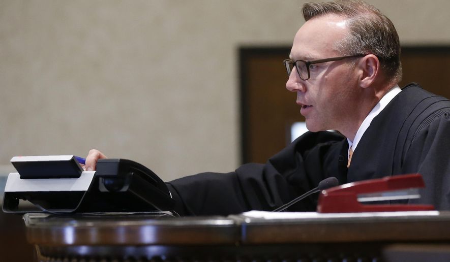 Judge Thad Balkman adjusts a telephone on the bench so that State's attorney Brad Beckworth, who could not be present, can listen to a hearing in regard to the request of CBS News/60 Minutes to unseal certain documents relating to pleadings filed by Teva Pharmaceutical Industries and Cephalon and associated companies, in Norman, Okla., Monday, Aug. 19, 2019. (AP Photo/Sue Ogrocki, Pool)