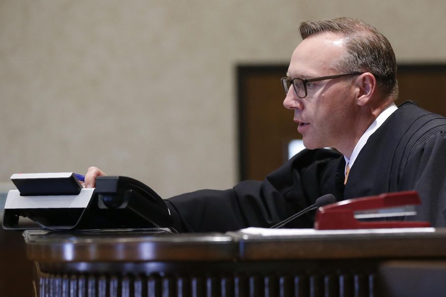 Judge Thad Balkman adjusts a telephone on the bench so that State's attorney Brad Beckworth, who could not be present, can listen to a hearing in regard to the request of CBS News/60 Minutes to unseal certain documents relating to pleadings filed by Teva Pharmaceutical Industries and Cephalon and associated companies, in Norman, Okla., Monday, Aug. 19, 2019. (AP Photo/Sue Ogrocki, Pool)