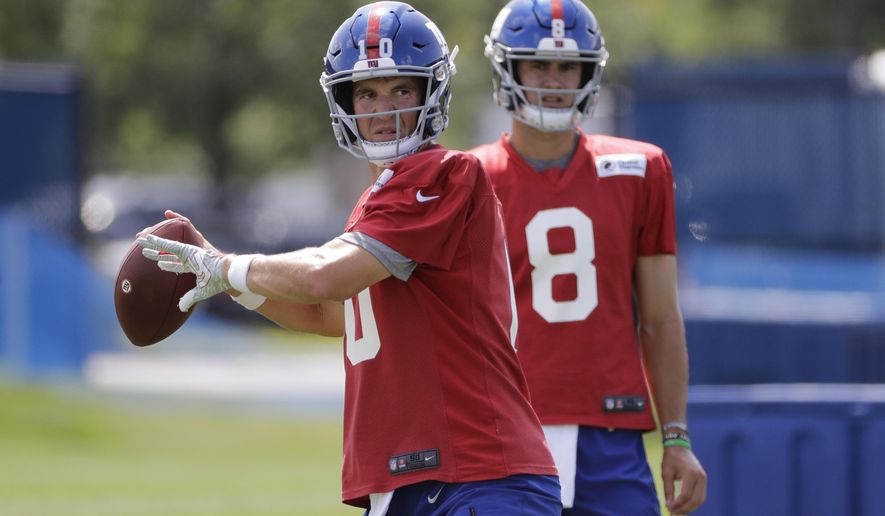 FILE - In this July 25, 2019, file photo, New York Giants' quarterback Eli Manning throws a pass as Daniel Jones watches at the NFL football team's training camp in East Rutherford, N.J. Eli Manning is entering a team-record 16th season with the New York Giants and his career in some ways might be coming full cycle. (AP Photo/Frank Franklin II, File)