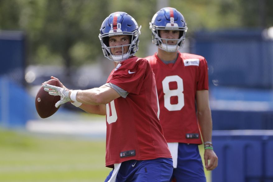 FILE - In this July 25, 2019, file photo, New York Giants' quarterback Eli Manning throws a pass as Daniel Jones watches at the NFL football team's training camp in East Rutherford, N.J. Eli Manning is entering a team-record 16th season with the New York Giants and his career in some ways might be coming full cycle. (AP Photo/Frank Franklin II, File)