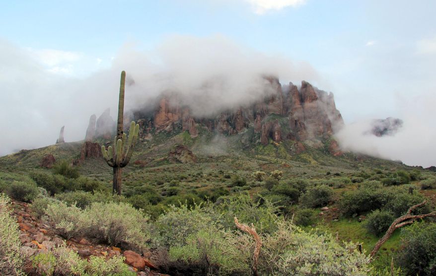 FILE - In this Jan. 29, 2015 file photo, low-hanging winter clouds hug part of Superstition Mountain in Lost Dutchman State Park in Apache Junction, Ariz. Summer is a different story. Authorities said Friday, Aug. 23, 2019 that 44 members of an out-of-state hiking group had to be rescued from the Phoenix trail after being overcome by heat that reached 106 degrees Fahrenheit Thursday. Superstition Fire & Medical District officials say two hikers were flown out by helicopter while others were able to walk back down with assistance. (AP Photo/Ted Shaffrey, File)
