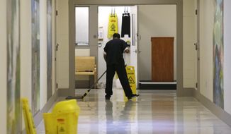FILE - In this June 21, 2017, file photo, a detainee mops a floor in a hallway of the Northwest Detention Center in Tacoma, Wash., during a media tour of the facility.  The Trump administration is opposing Washington state’s effort to make a privately run, for-profit immigration jail pay detainees minimum wage for the work they do. Washington Attorney General Bob Ferguson sued The GEO Group in 2017, saying its Northwest Detention Center in Tacoma must pay the state minimum wage to detainees who perform kitchen, janitorial and other tasks. (AP Photo/Ted S. Warren, File)