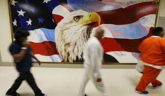 FILE - In June 21, 2017, file photo, detainees walk past a mural in the Northwest Detention Center in Tacoma, Wash., during a media tour of the facility. The Trump administration is opposing Washington state’s effort to make a privately run, for-profit immigration jail pay detainees minimum wage for the work they do. Washington Attorney General Bob Ferguson sued The GEO Group in 2017, saying its Northwest Detention Center in Tacoma must pay the state minimum wage to detainees who perform kitchen, janitorial and other tasks. (AP Photo/Ted S. Warren, File)