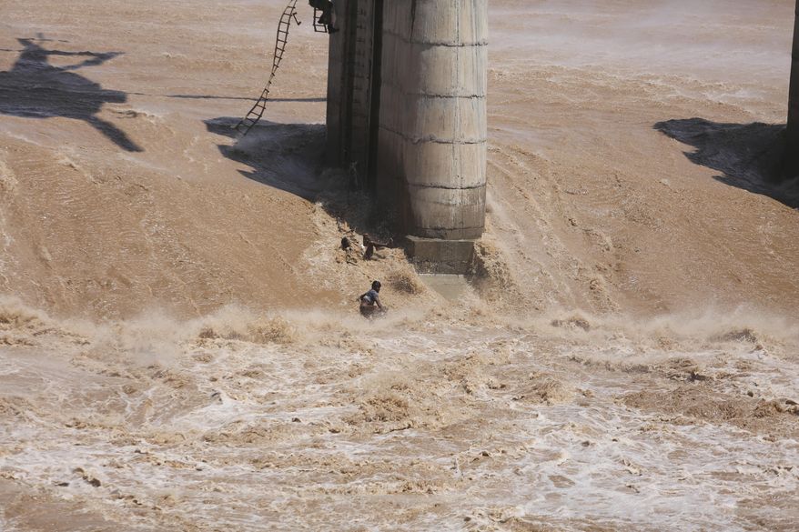 In this Monday, Aug. 19, 2019, file photo, two Indian fishermen fall in floodwaters after a rope broke during a failed rescue operation using an Indian Air Force helicopter in the River Tawi in Jammu, India. Both the fishermen later swam to safety. Water levels in many rivers in north India have risen following heavy monsoon rains. (AP Photo/Channi Anand, File)
