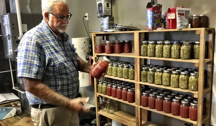 Neil Rudy pulls a jar of tomato juice off a shelf in his garage in West Daviess County, KY., where he keeps the canned vegetables that he and his wife, Vicky, store. The Rudys canned tomato juice and green beans this years, combining for nearly 200 quarters that will last through until next season. (Don Wilkins/The Messenger-Inquirer via AP)