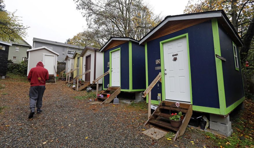 In this Nov. 9, 2017, file photo, a resident walks past a row of tiny houses at a homeless encampment. A real estate company in San Diego is listing a repurposed shed in a residential backyard as a two-bedroom studio apartment. The company is asking a little over $1,000/month for the air-conditioned rental. LINK for listing: https://www.zumper.com/apartment-buildings/p411204/4733-35-oregon-st-north-park-san-diego-ca (AP Photo/Elaine Thompson, File) **FILE**