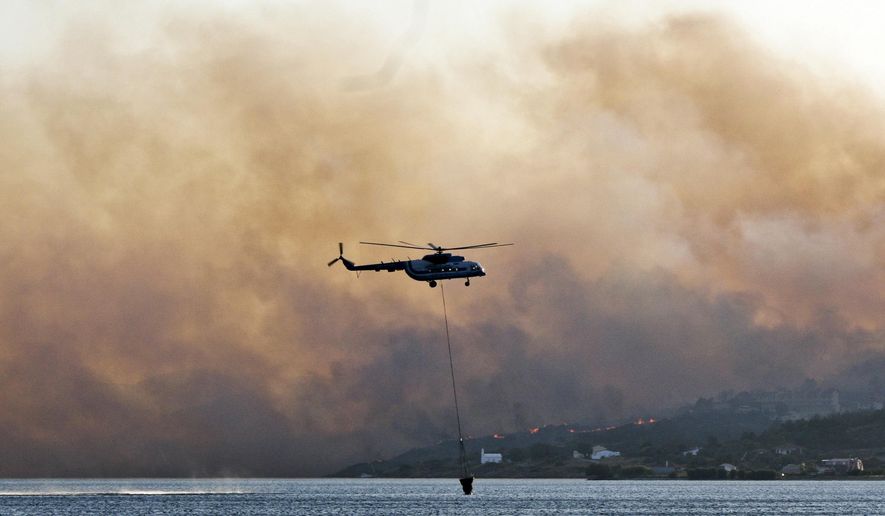 In this Saturday, Aug. 24, 2019 photo shows an helicopter fills its bucket with water during a wildfire near Pythagorio town on the eastern Greek island of Samos. Authorities evacuated two hotels and house the customers in an arena in the town of Pythagorio. Hot, dry weather and high winds helped fuel a total of 68 wildfires across Greece Saturday and the situation will remain dangerous Sunday. (AP Photo/Michael Svarnias)