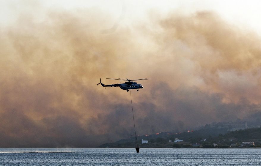 In this Saturday, Aug. 24, 2019 photo shows an helicopter fills its bucket with water during a wildfire near Pythagorio town on the eastern Greek island of Samos. Authorities evacuated two hotels and house the customers in an arena in the town of Pythagorio. Hot, dry weather and high winds helped fuel a total of 68 wildfires across Greece Saturday and the situation will remain dangerous Sunday. (AP Photo/Michael Svarnias)