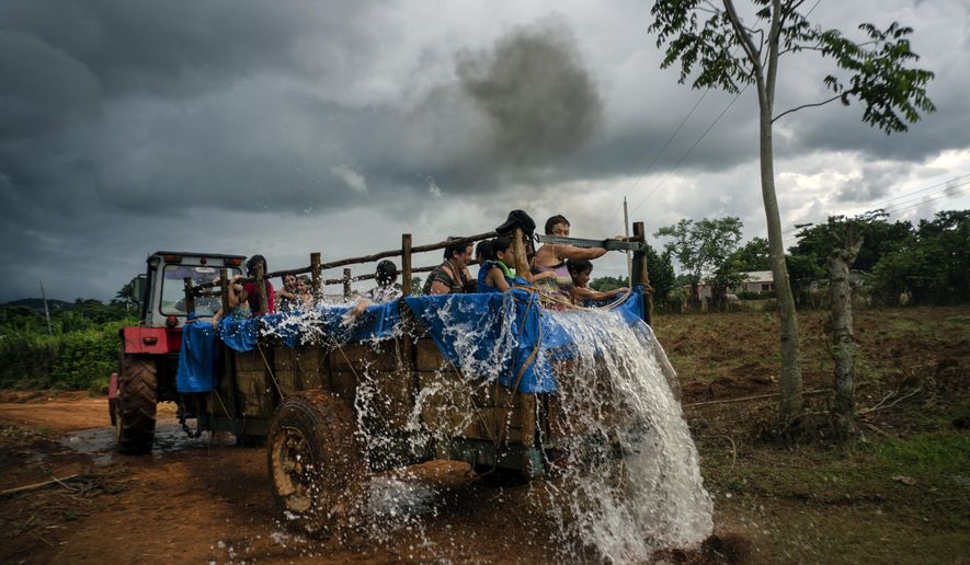 In this Aug. 24, 2019 photo, a tractor pulls a trailer that was converted into a swimming pool as it drives along the roads of El Infernal neighborhood in San Andres in the province of Pinar del Río, Cuba. The idea for the mobile tractor-pool was hatched by local parents, to make their kids happy and fight the harsh Caribbean heat. (AP Photo/Ramon Espinosa)