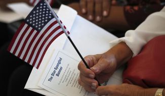 In this Aug. 16, 2019, file photo a citizen candidate holds an American flag and the words to The Star-Spangled Banner before the start of a naturalization ceremony at the U.S. Citizenship and Immigration Services Miami field office in Miami. (AP Photo/Wilfredo Lee) ** FILE **