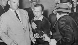 FILE - In this Nov. 24, 1963 file photo, Lee Harvey Oswald reacts as Dallas night club owner Jack Ruby, foreground, shoots at him from point blank range in a corridor of Dallas police headquarters At left is Detective Jim Leavelle. The longtime Dallas lawman who was captured in one of history&#39;s most iconic photographs as he escorted President John F. Kennedy&#39;s assassin moments before he was fatally shot, has died on Thursday, Aug. 29, 2019. He was 99. (Bob Jackson/Dallas Times-Herald via AP)