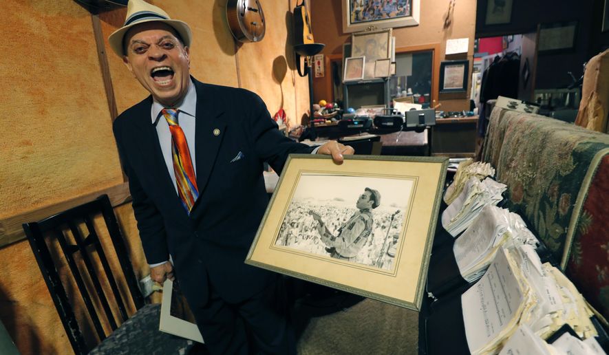 In this Wednesday, Aug. 28, 2019 photo Deacon John Moore shows a photo of himself performing at the New Orleans Pop Festival, in his home in New Orleans. Fifty years ago, a couple weeks after the Woodstock music festival drew hundreds of thousands to farmland in New York, there was a smaller, bayou-country re-enactment of sorts. It was called the New Orleans Pop Festival, although it took place 60 miles away, it featured several of the same acts as Woodstock. Also on hand was Deacon John, who at 78 is still a renowned New Orleans performer. (AP Photo/Gerald Herbert)
