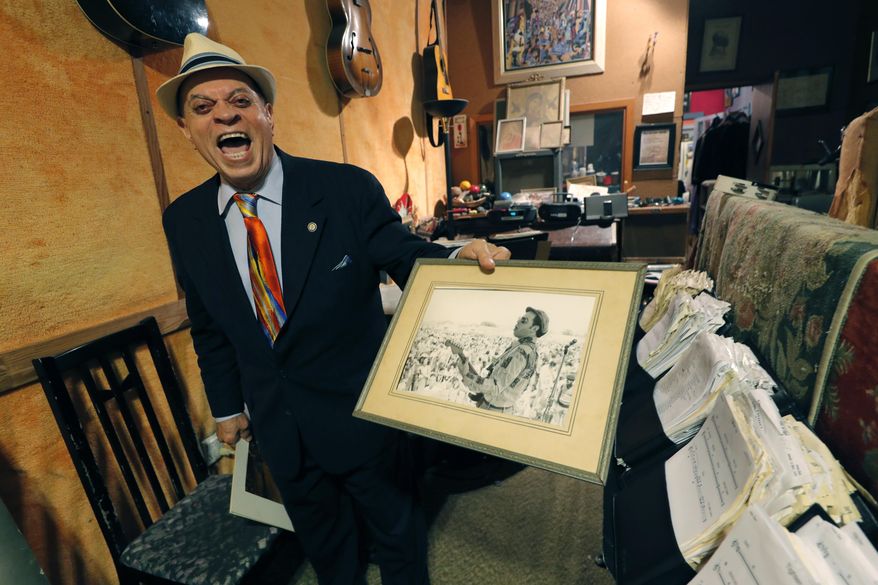 In this Wednesday, Aug. 28, 2019 photo Deacon John Moore shows a photo of himself performing at the New Orleans Pop Festival, in his home in New Orleans. Fifty years ago, a couple weeks after the Woodstock music festival drew hundreds of thousands to farmland in New York, there was a smaller, bayou-country re-enactment of sorts. It was called the New Orleans Pop Festival, although it took place 60 miles away, it featured several of the same acts as Woodstock. Also on hand was Deacon John, who at 78 is still a renowned New Orleans performer. (AP Photo/Gerald Herbert)