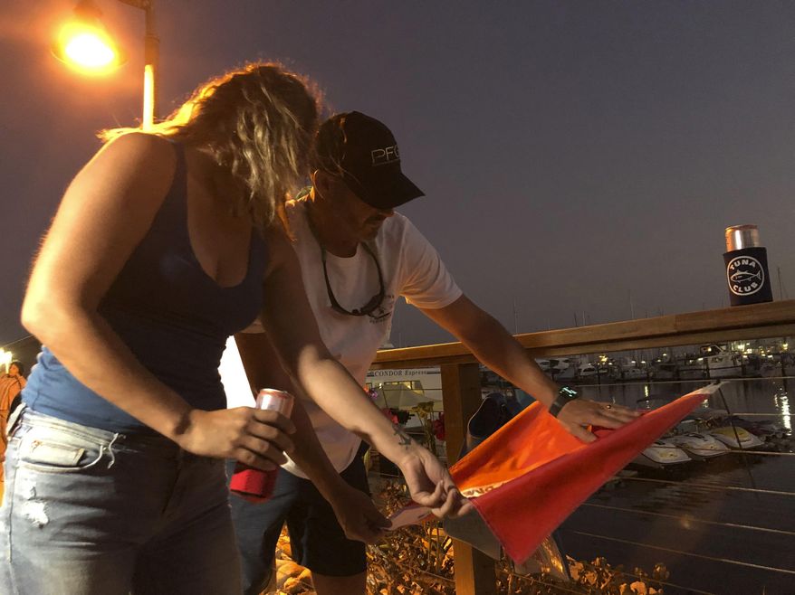 JJ Lambert, 38, and his fiancee, Jenna Marsala, 33, hang up a dive flag in remembrance of the victims of the Conception boat fire at a memorial site on Monday, Sept. 2, 2019, in Santa Barbara, Calif. A fire raged through the boat carrying recreational scuba divers anchored near an island off the Southern California coast early Monday, leaving multiple people dead and hope diminishing that any of the more than two dozen people still missing would be found alive. (AP Photo/Stefanie Dazio)