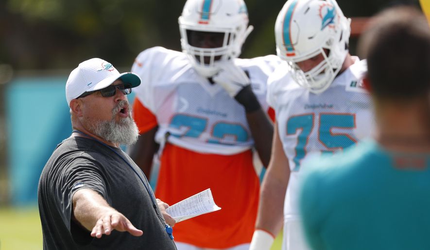 FILE - In this July 30, 2019, file photo, Miami Dolphins offensive line coach Dave DeGuglielmo, left, runs players through drills at the teams NFL football training camp, in Davie, Fla. As part of rookie coach Brian Flores’ staff, offensive line coach Dave DeGuglielmo is trying to clean up a mess for the Miami Dolphins, which is nothing new. DeGuglielmo also was a Dolphins assistant in 2009-11, and for the last part of 2017. “I really like it here,” he said Tuesday, Sept. 3, 2019. “I’m like a stray dog _ they keep feeding me, I keep coming back.”(AP Photo/Wilfredo Lee, File)