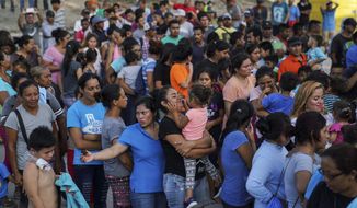 In this Aug. 30, 2019, photo, migrants, many who were returned to Mexico under the Trump administration’s “Remain in Mexico,” program wait in line to get a meal in an encampment near the Gateway International Bridge in Matamoros. Many shelters at the Mexico border are at or above capacity already, and some families have been sleeping in tents or on blankets in the blistering summer heat. (AP Photo/Veronica G. Cardenas)