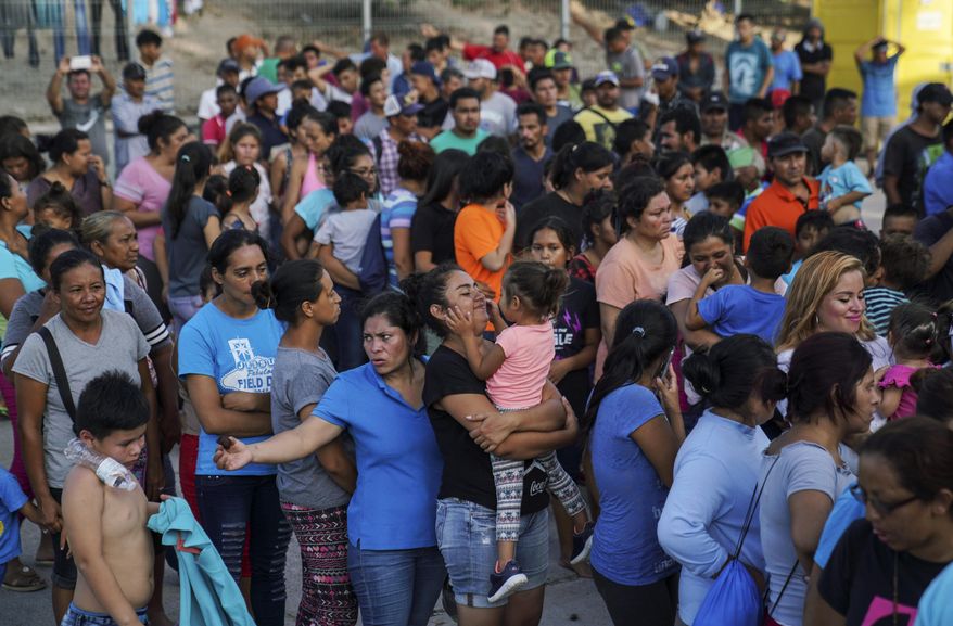 In this Aug. 30, 2019, photo, migrants, many who were returned to Mexico under the Trump administration’s “Remain in Mexico,” program wait in line to get a meal in an encampment near the Gateway International Bridge in Matamoros. Many shelters at the Mexico border are at or above capacity already, and some families have been sleeping in tents or on blankets in the blistering summer heat. (AP Photo/Veronica G. Cardenas)