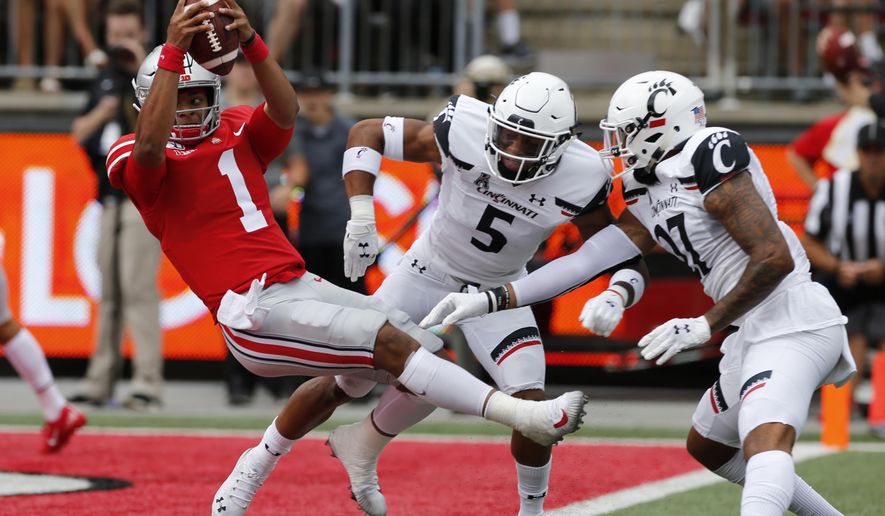 Ohio State quarterback Justin Fields, left, dives over the goal line past Cincinnati defensive back Darrick Forrest, center, and linebacker Dorian Holloway during the first half of an NCAA college football game Saturday, Sept. 7, 2019, in Columbus, Ohio. (AP Photo/Jay LaPrete)