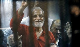 FILE - In this file photo dated Saturday, May 16, 2015, Muslim Brotherhood spiritual leader, Mohammed Badie waves from a defendants cage in a makeshift courtroom at the national police academy, in eastern Cairo, Egypt.  An Egyptian court on Saturday, Sept. 7, 2019,  sentenced 11 people to life in prison, including Mohammed Badie, after a retrial on charges related to mass prison breaks at the height of the 2011 popular uprising.  The retrial was related to a case rooted in the escape of 20,000 inmates from Egyptian prisons in Jan. 2011, early in the 18-day uprising that toppled longtime autocratic President Hosni Mubarak, who had testified in the case in December last year. The verdict cannot be appealed.  (AP Photo/Ahmed Omar, FILE)